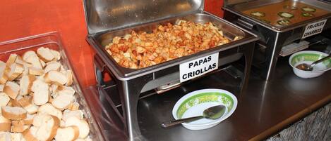 A buffet with labeled food items including papas criollas, charros, and bread.