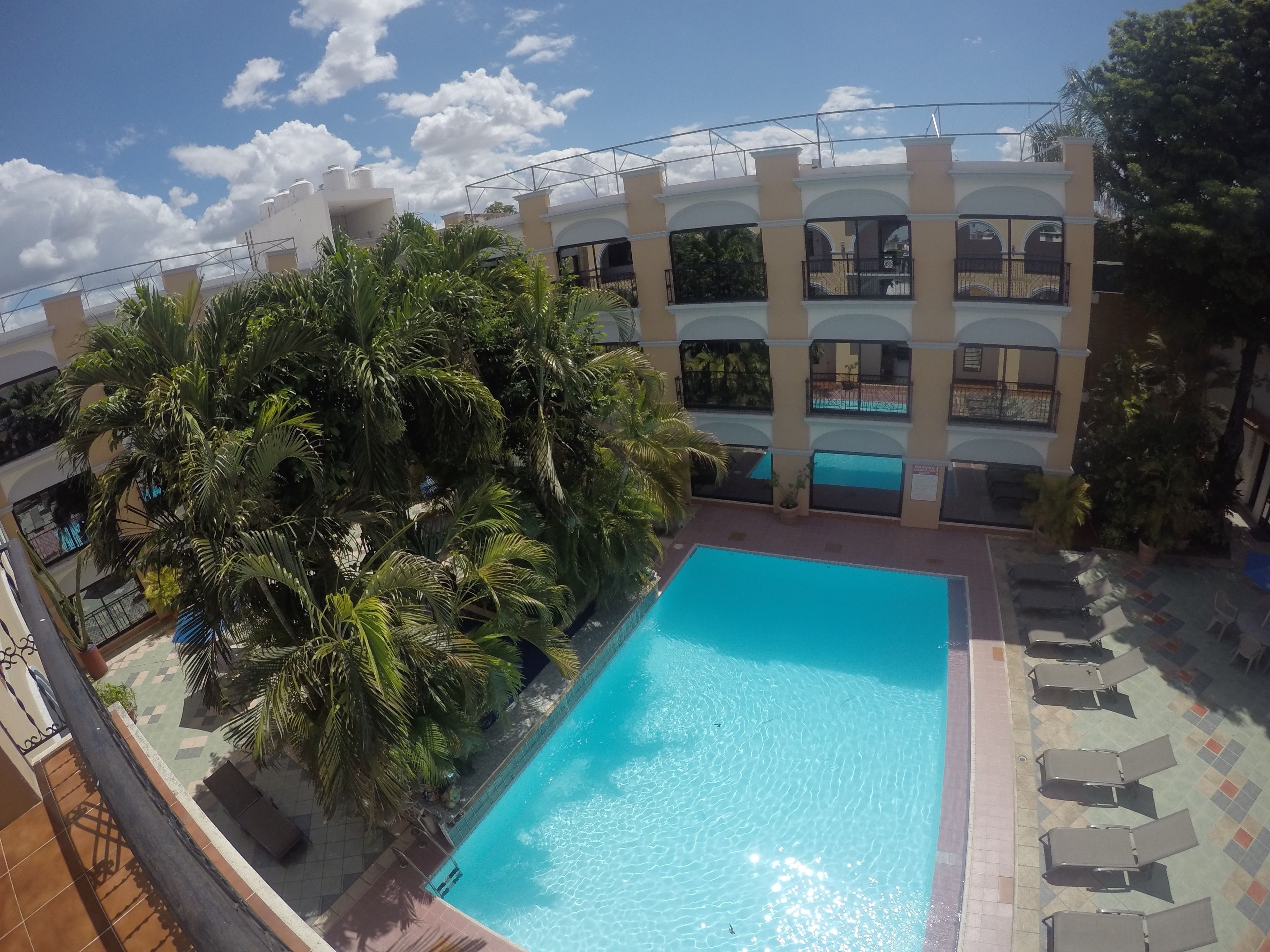 A swimming pool surrounded by palm trees and a multi-story building with balconies.