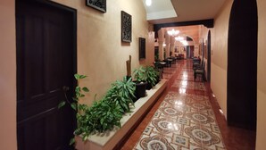 A corridor with a tiled floor, potted plants, framed artwork, and a seating area with tables and chairs. - Hotel Doralba Inn (Mérida)
