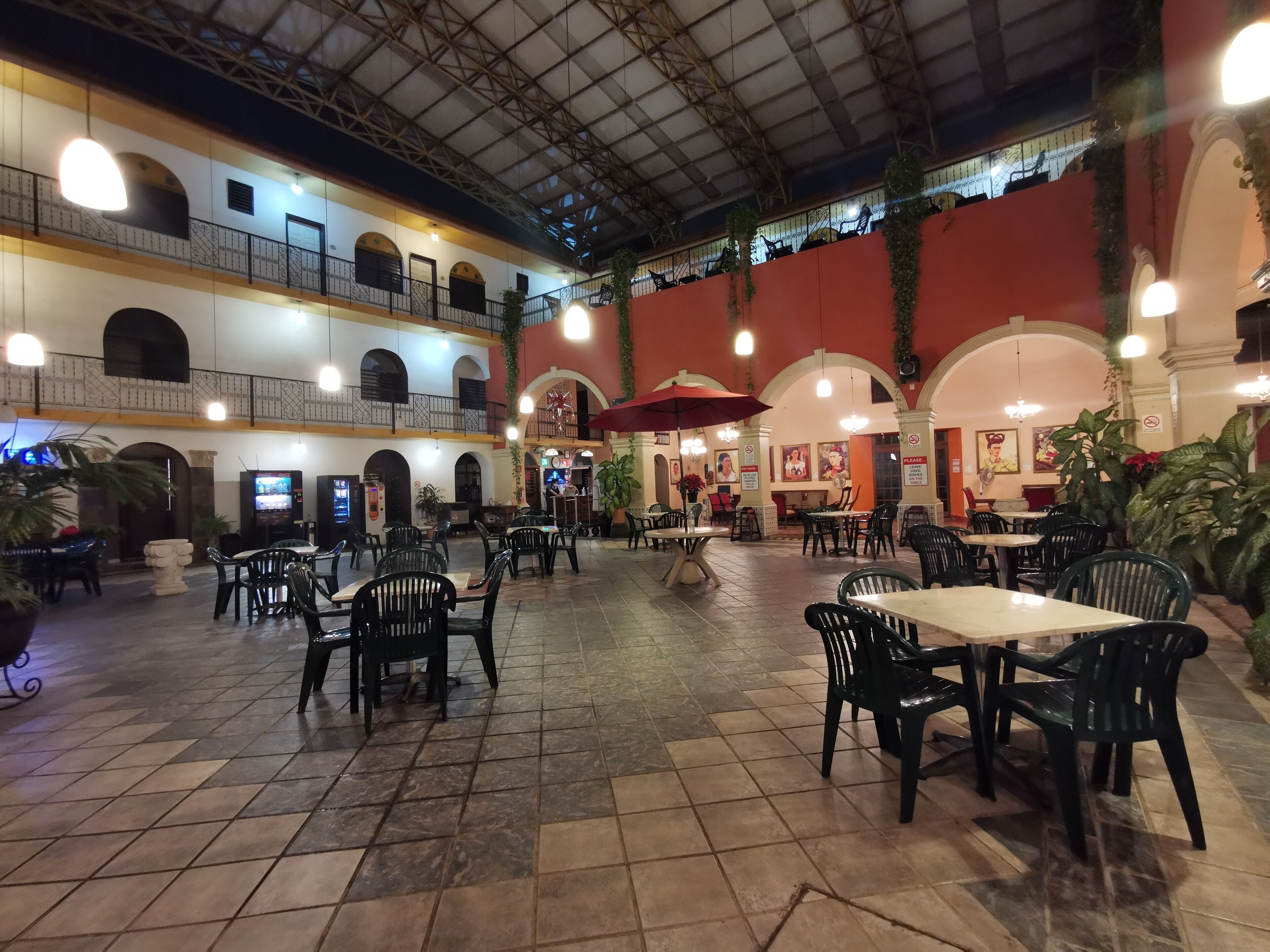 Un vaste espace intérieur aménagé en salle à manger, avec de nombreuses tables et chaises, un plafond haut doté d’une structure métallique et une décoration aux couleurs rouge et blanche.