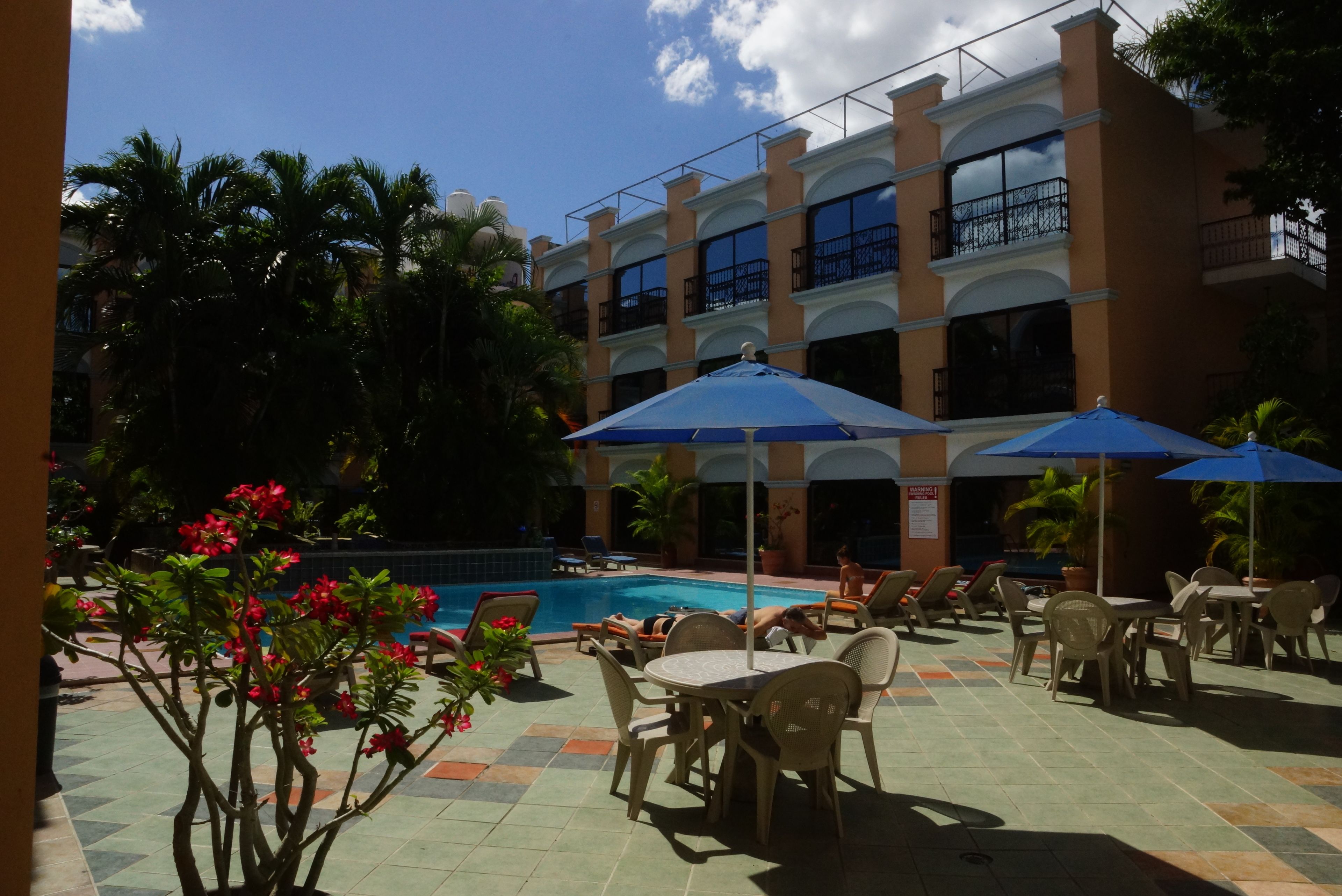 A hotel courtyard with a swimming pool, outdoor seating, and a multi-story building with balconies.