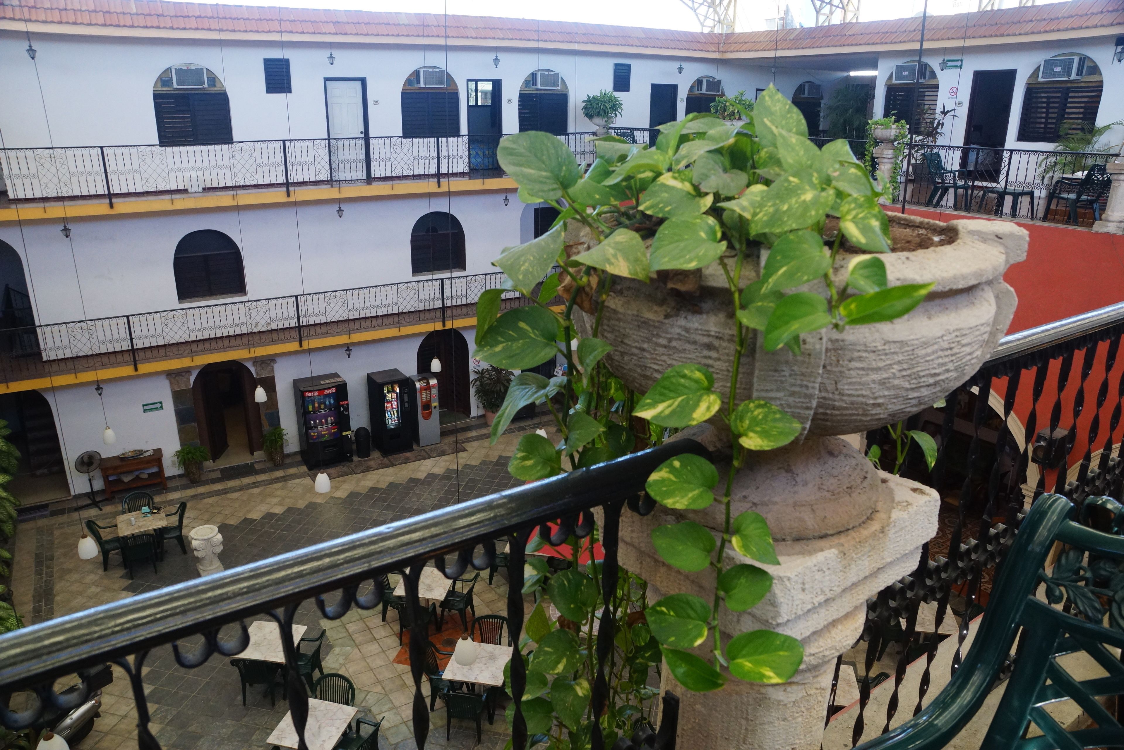 Um pátio com área de estar externa, um vaso de pedra com planta e um edifício com várias janelas e varandas.