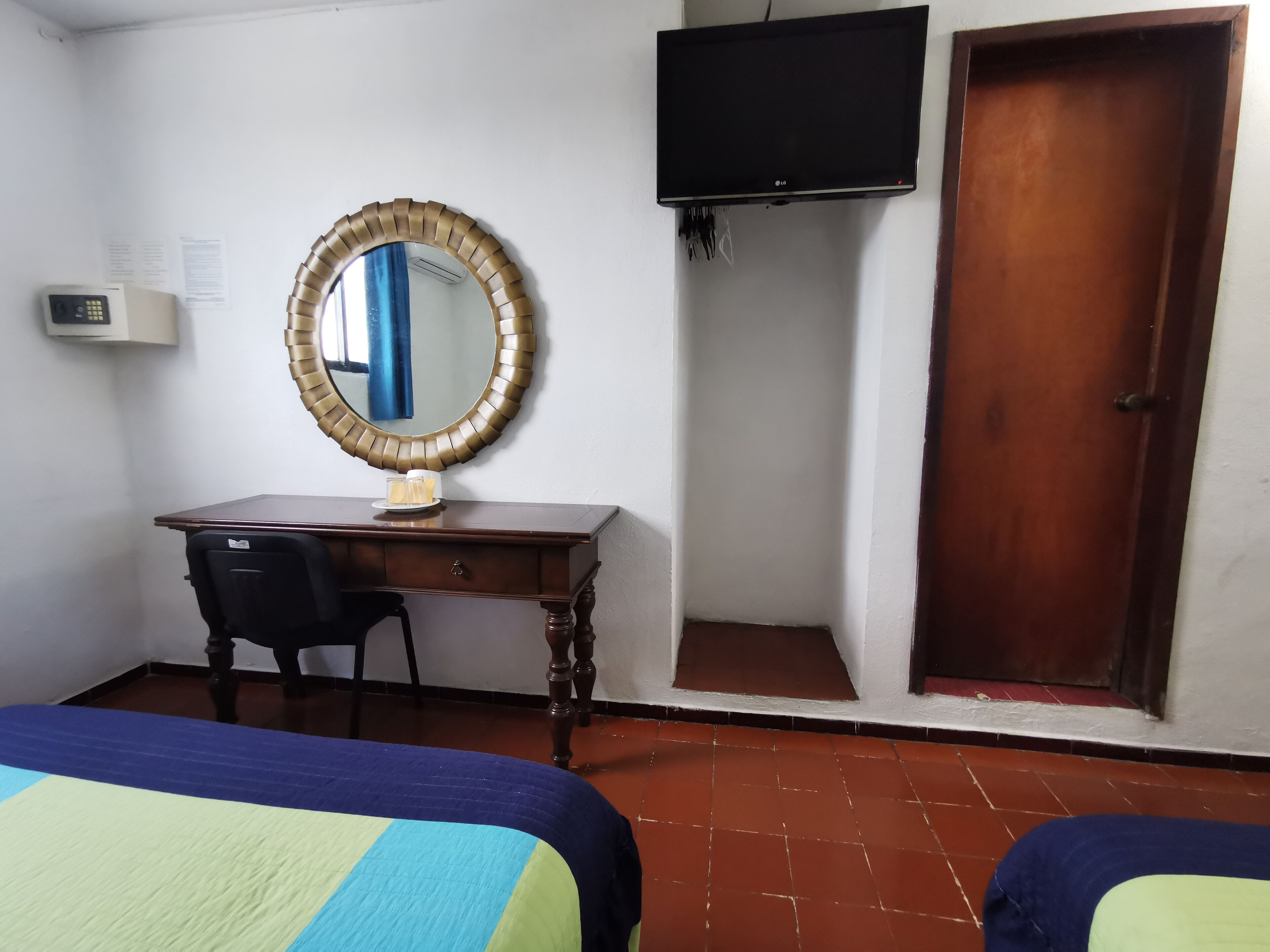 Una stanza con un letto, una scrivania con una sedia, uno specchio, una televisione e una porta.