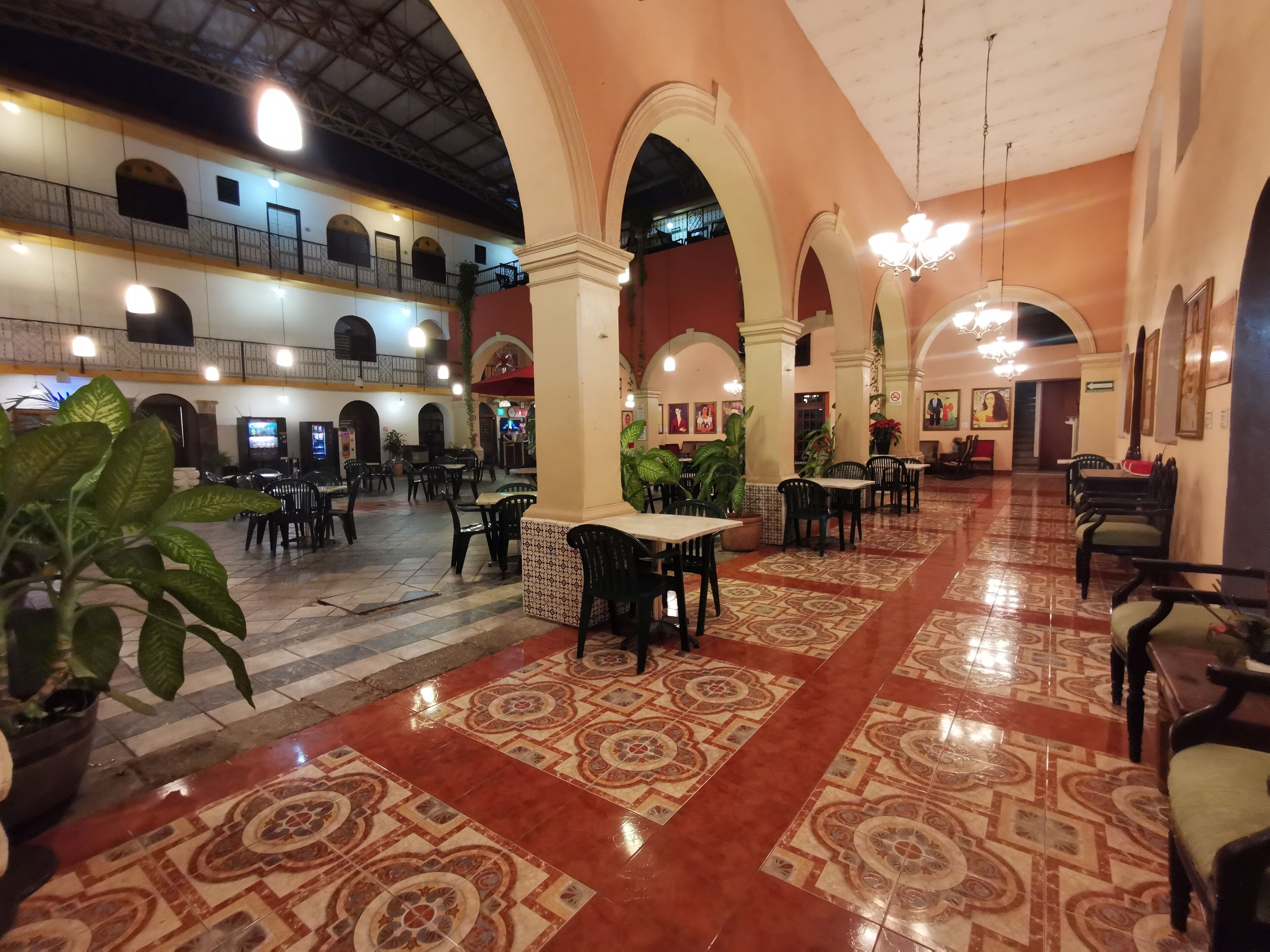 A spacious indoor area with multiple dining tables and chairs, large decorative pillars, and a high ceiling with exposed beams.