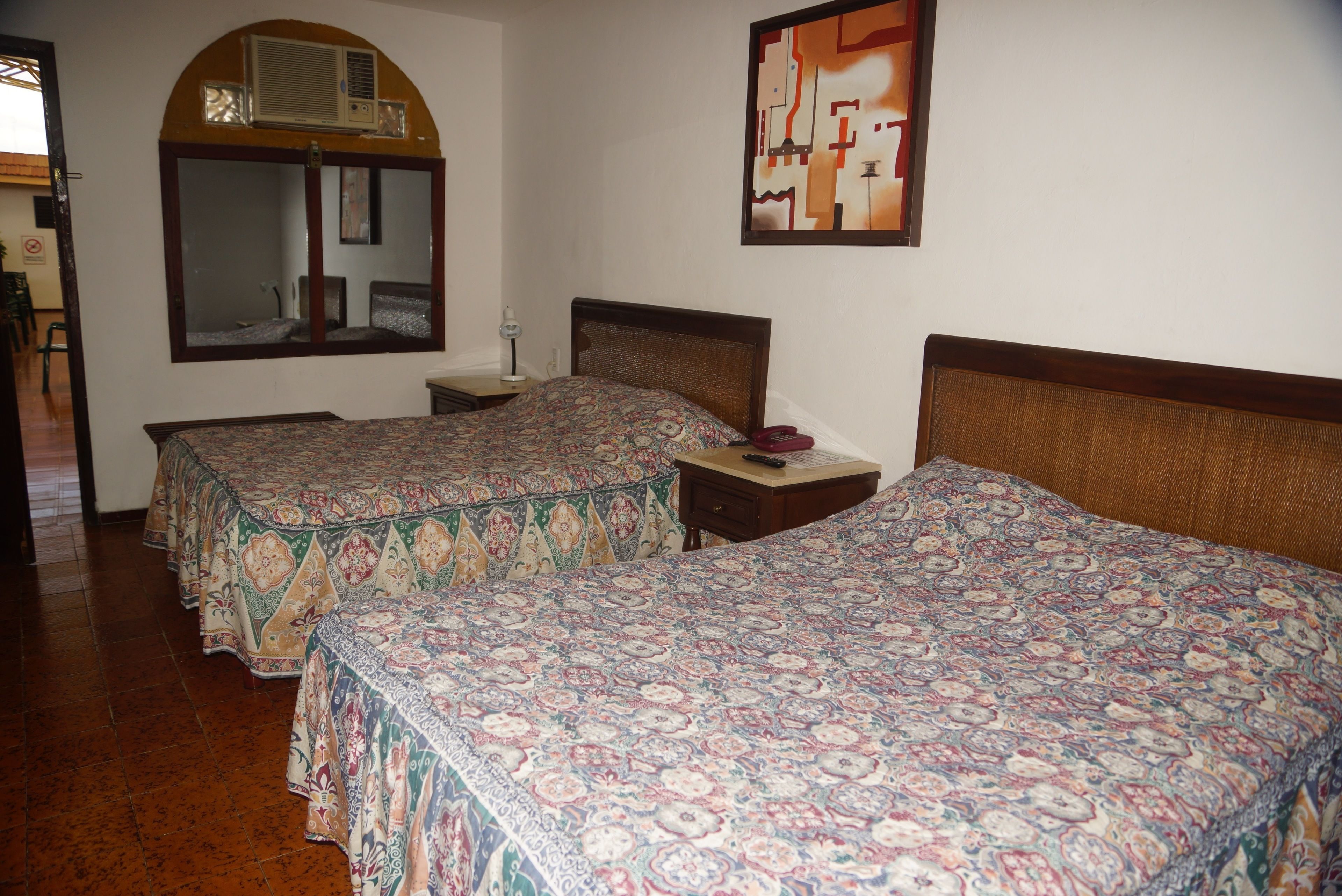 Habitación de hotel con dos camas, un espejo grande, una mesita y un aire acondicionado instalado en la pared.