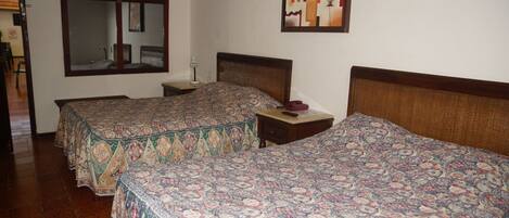 Habitación de hotel con dos camas, un espejo grande, una mesita y un aire acondicionado instalado en la pared.