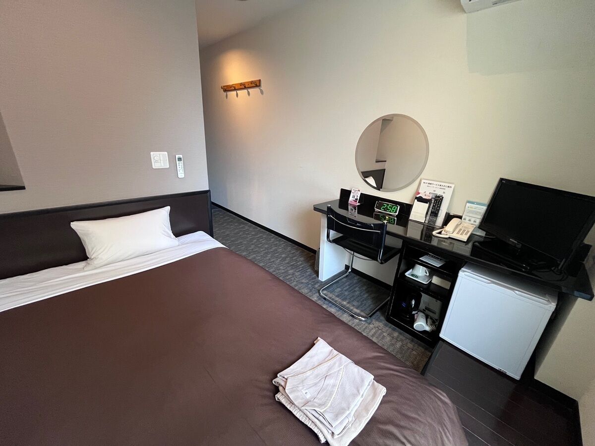 A hotel room with a large bed, a desk with a computer, a TV, and a small fridge.