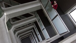 A modern interior with a geometric design, featuring a glass railing and a person standing by it. - Urbain Hiroshima Executive (Hiroshima)