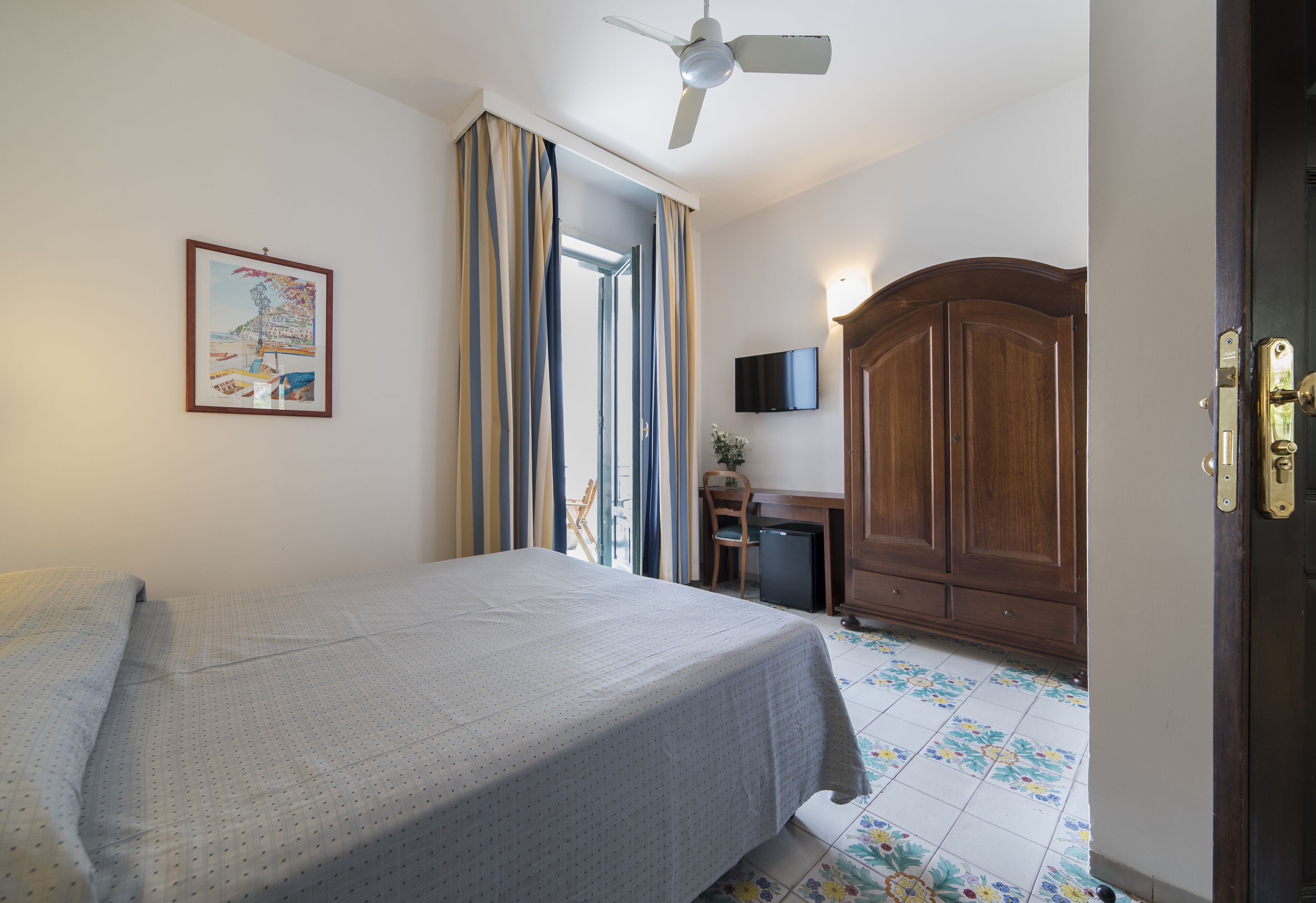 Quarto com cama, escrivaninha, televisão e guarda-roupa.