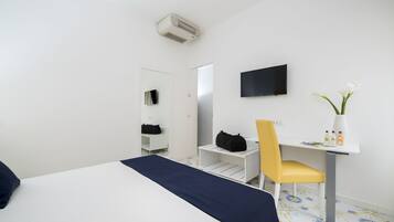 Habitación de hotel con cama, escritorio con silla, televisor, espejo y una pequeña mesa con un jarrón de flores.
