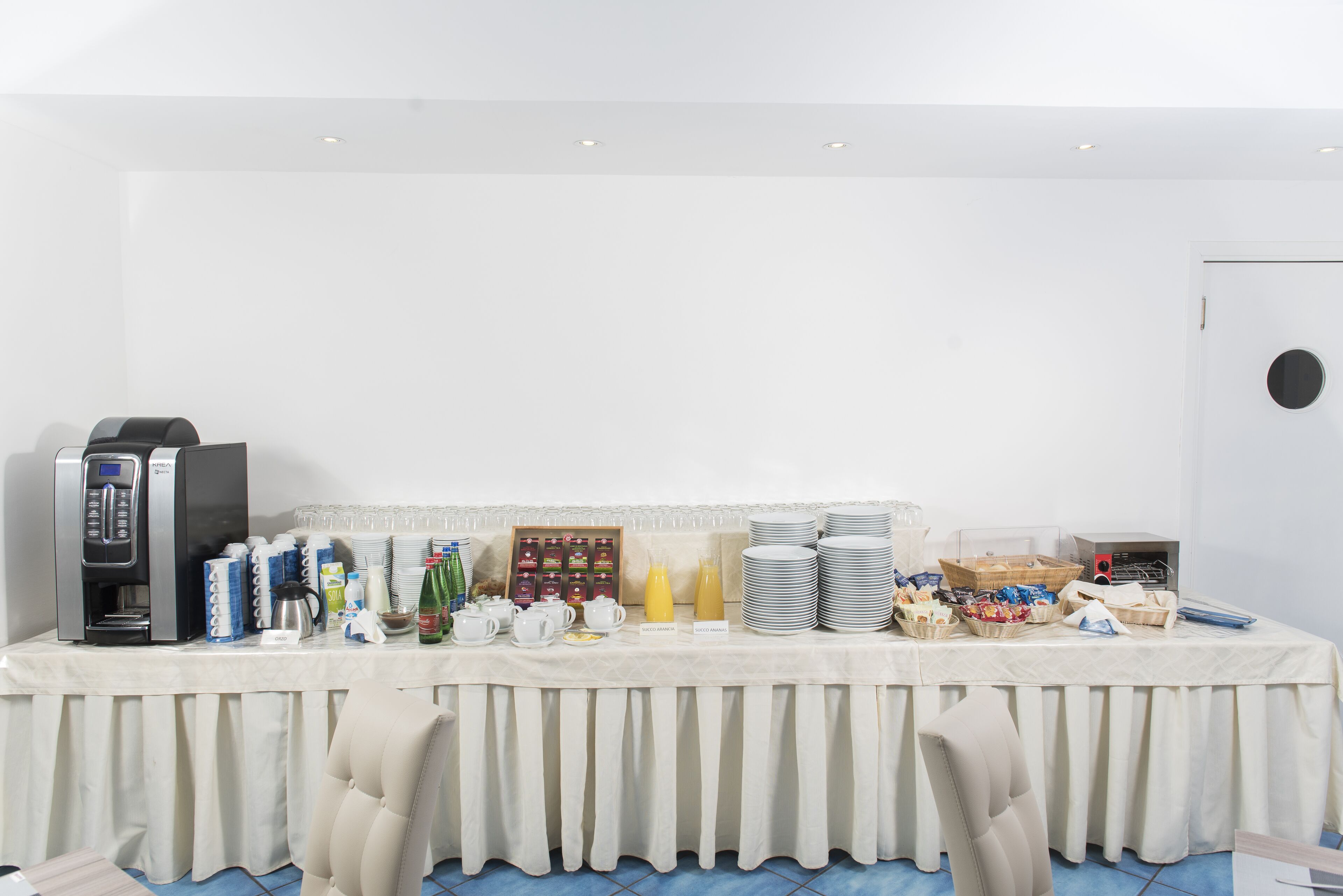 A buffet setup with a coffee machine, plates, cups, and various food items.