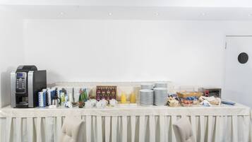 Una mesa de buffet con una máquina de café, platos, vasos y diversos alimentos.