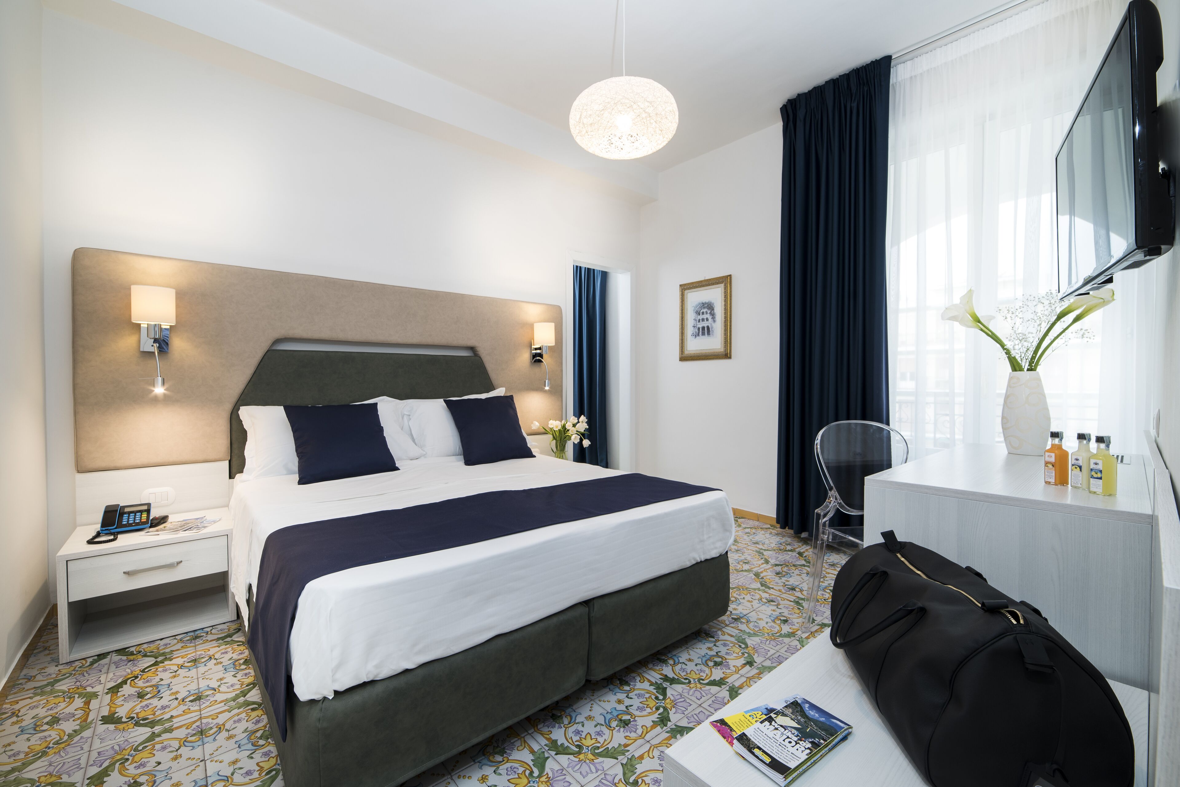 Habitación de hotel con una cama grande, mesitas de noche, un escritorio con silla, televisión y ventana con cortinas.