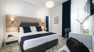 Habitación de hotel con una cama grande, mesitas de noche, un escritorio con silla, televisión y ventana con cortinas.