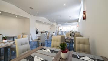 Een moderne eetruimte met meerdere tafels en stoelen, een centrale decoratieve plant en een plafond met inbouwverlichting.