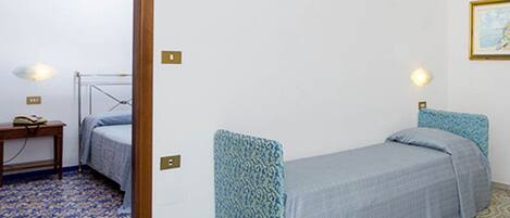 A small, single-bed room with patterned bedding, a bedside table, and wall-mounted lights.