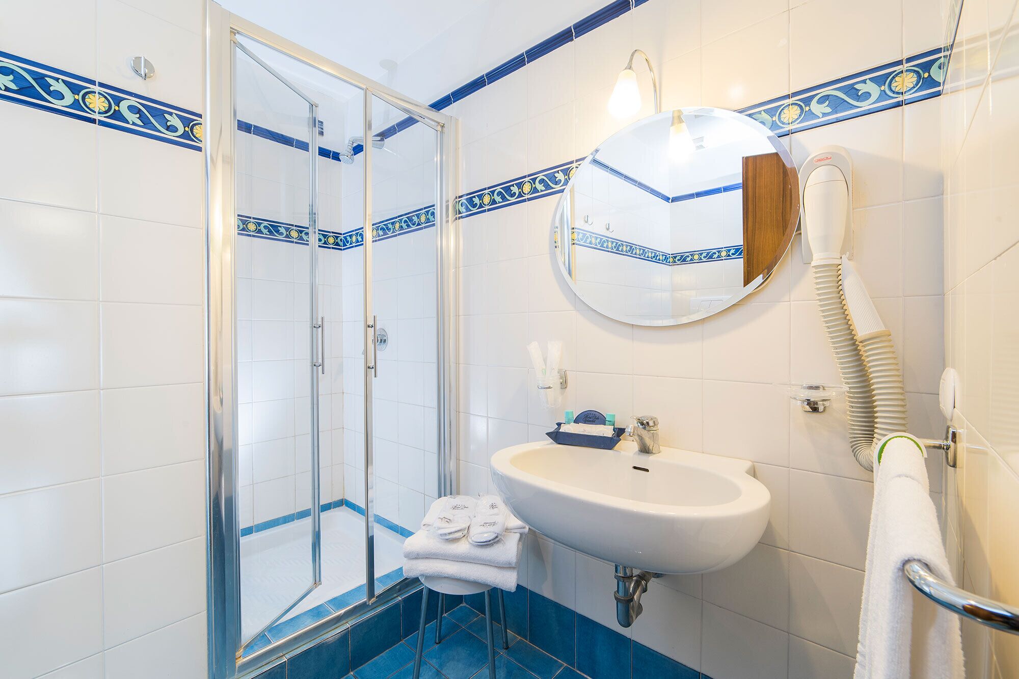 Un baño con cabina de ducha de vidrio, un lavabo con espejo y un perchero para toallas.