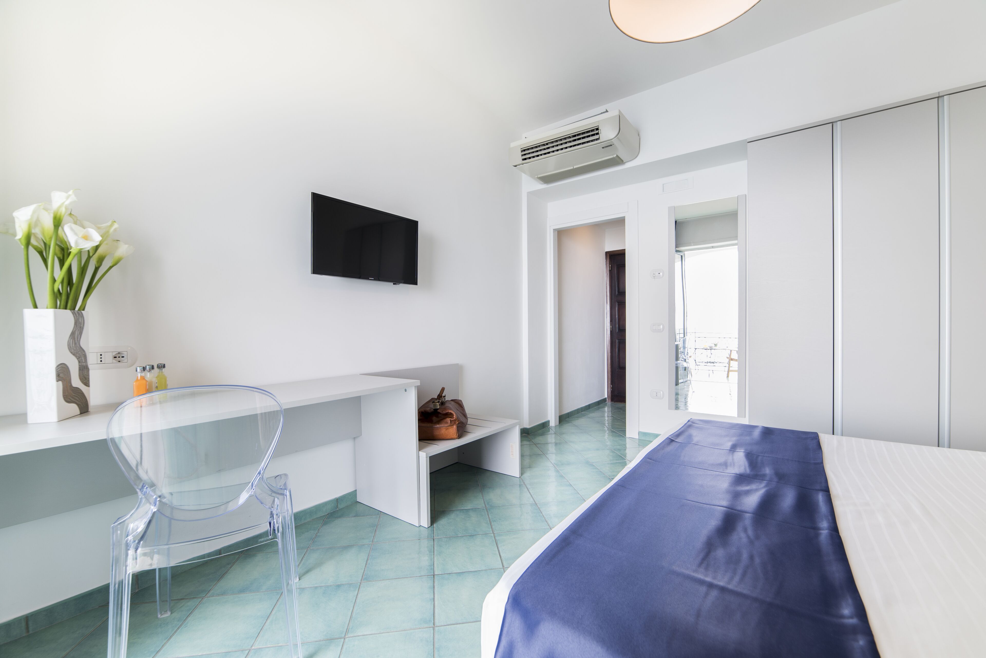 A modern hotel room with a bed, a desk with a chair, a flat-screen TV, and a view of the outdoors.