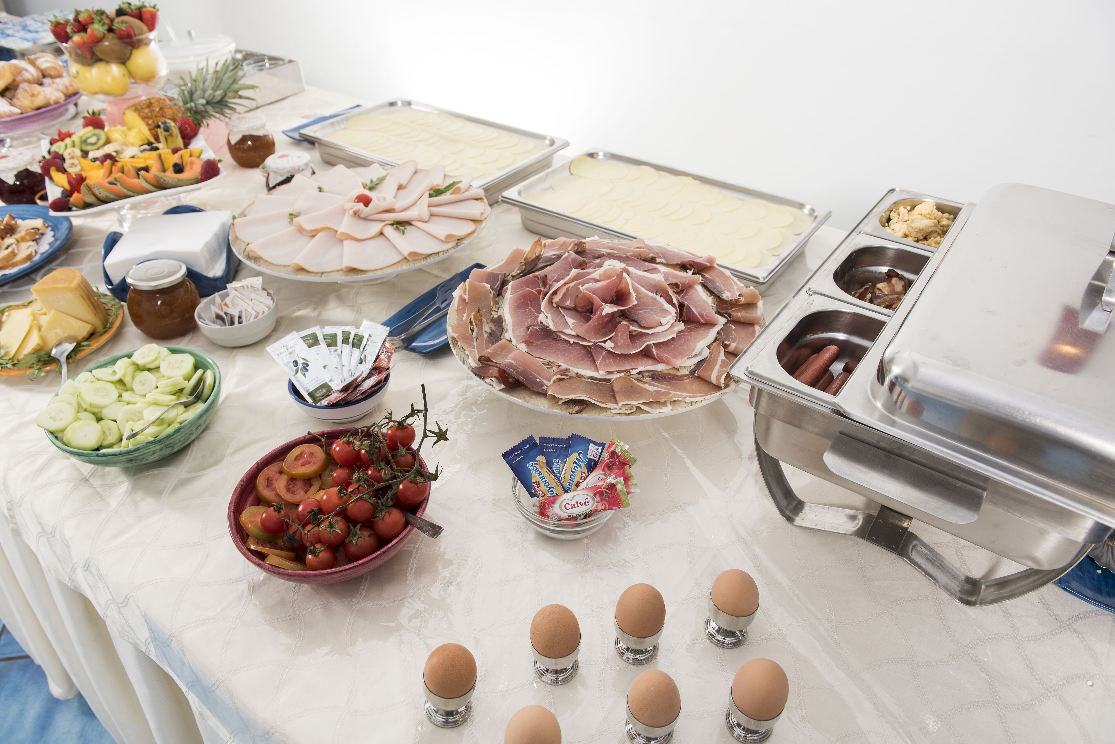 Une table de buffet proposant une variété d’aliments, notamment des viandes et des fromages en tranches, des fruits et des œufs.