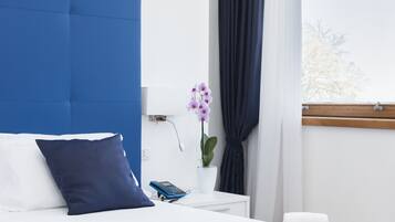 Cama bem arrumada com cabeceira azul, roupa de cama branca e almofada azul decorativa.