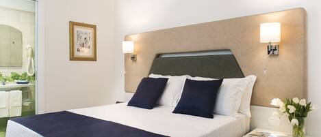 A neatly made bed with a dark blue bedspread and white linens, a bedside table with a lamp, and a framed picture on the wall.