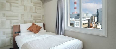 A hotel room with a bed, a window with a view of buildings, and a patterned wall.