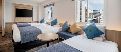Et hotelværelse med to senge, en sofa, et fjernsyn og udsigt over byen.