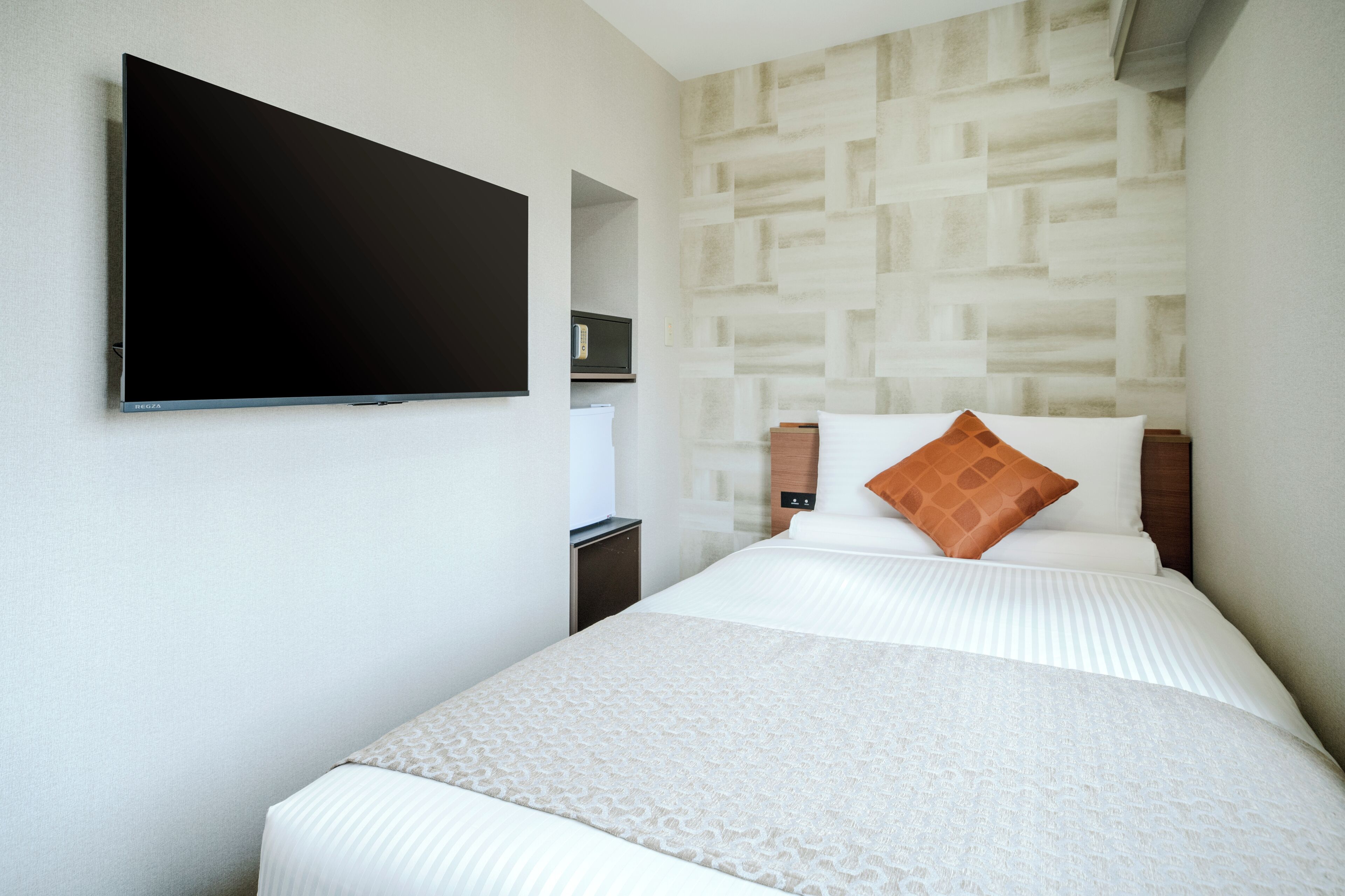 Quarto de hotel com cama, televisão de tela plana na parede, mesinha de cabeceira e cofre fixado na parede.