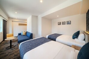 A hotel room with two beds, a sofa, a small table, and a wall with three framed pictures.