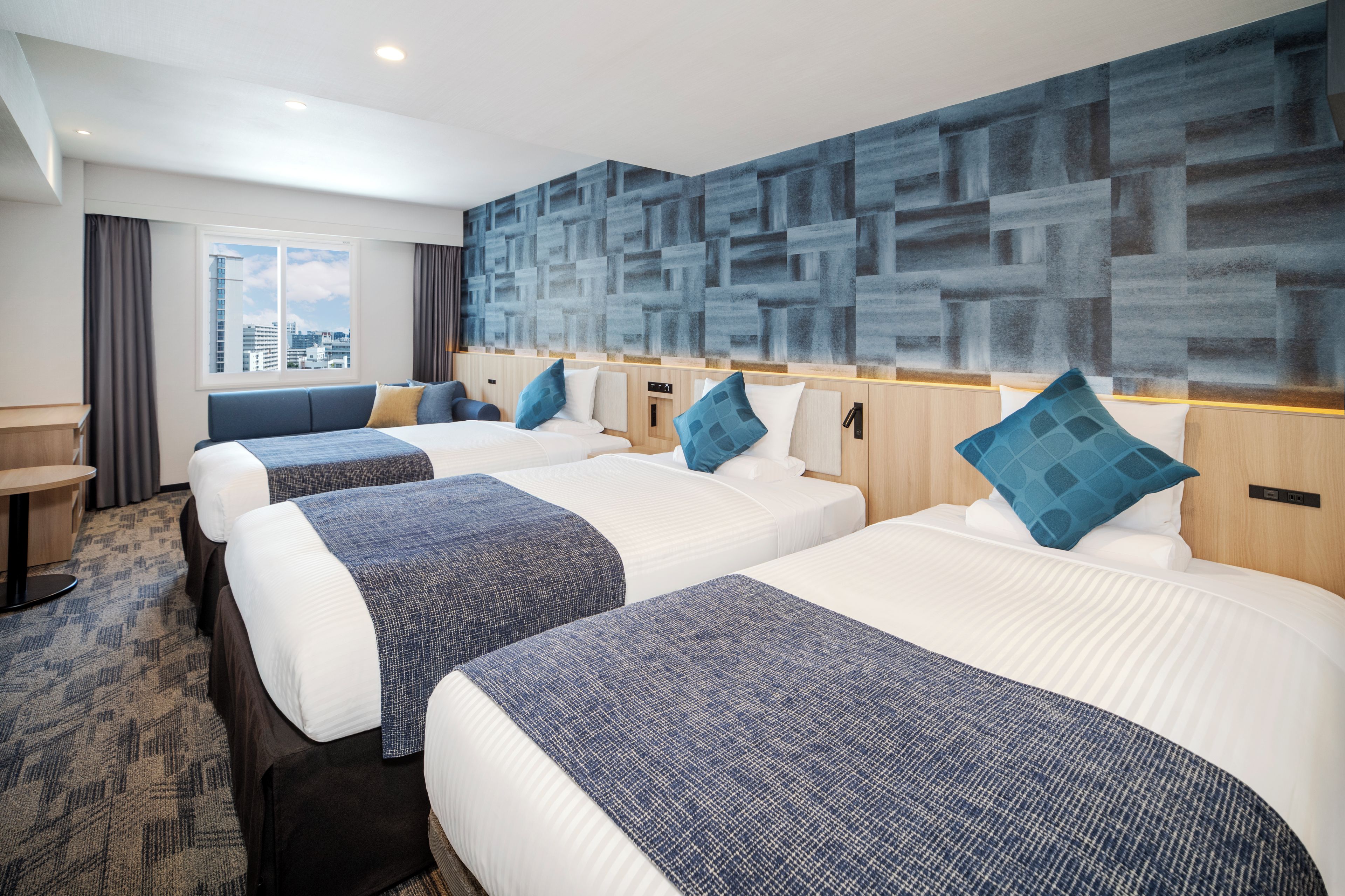 A hotel room with three beds, a view of the city, and a modern wall design.