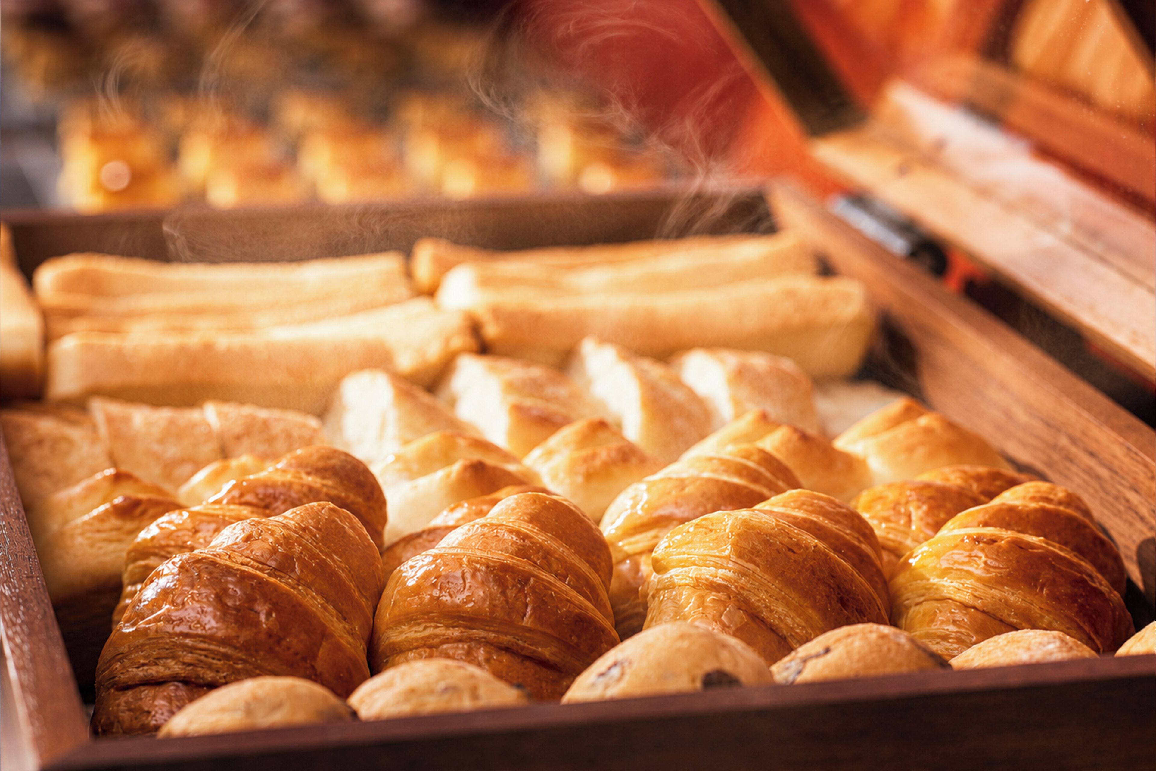 Diversos produtos de panificação, incluindo croissants e baguetes, expostos em uma caixa de madeira.