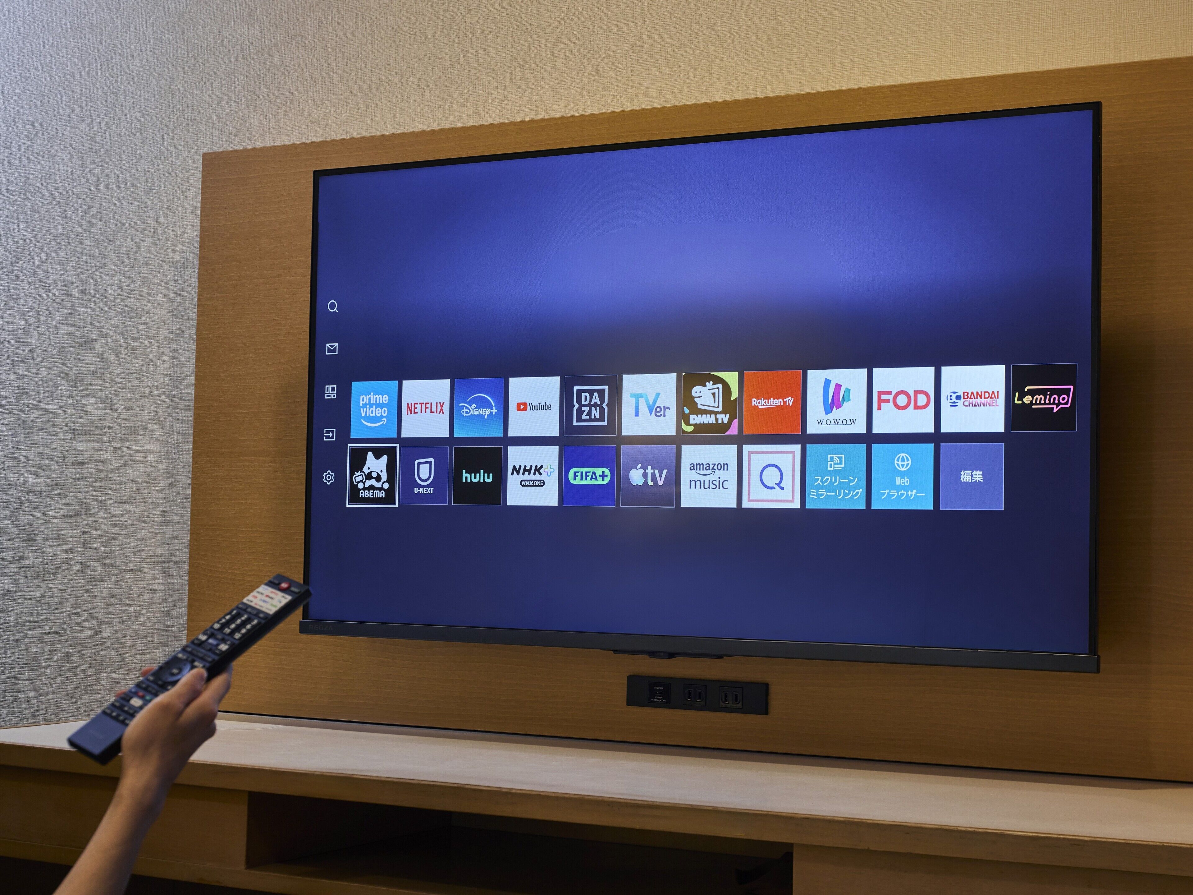 Un televisor montado en una pared de madera con un control remoto en la mano.