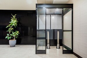 Un ascensor moderno con puerta de vidrio, una planta en maceta y un cesto de basura.
