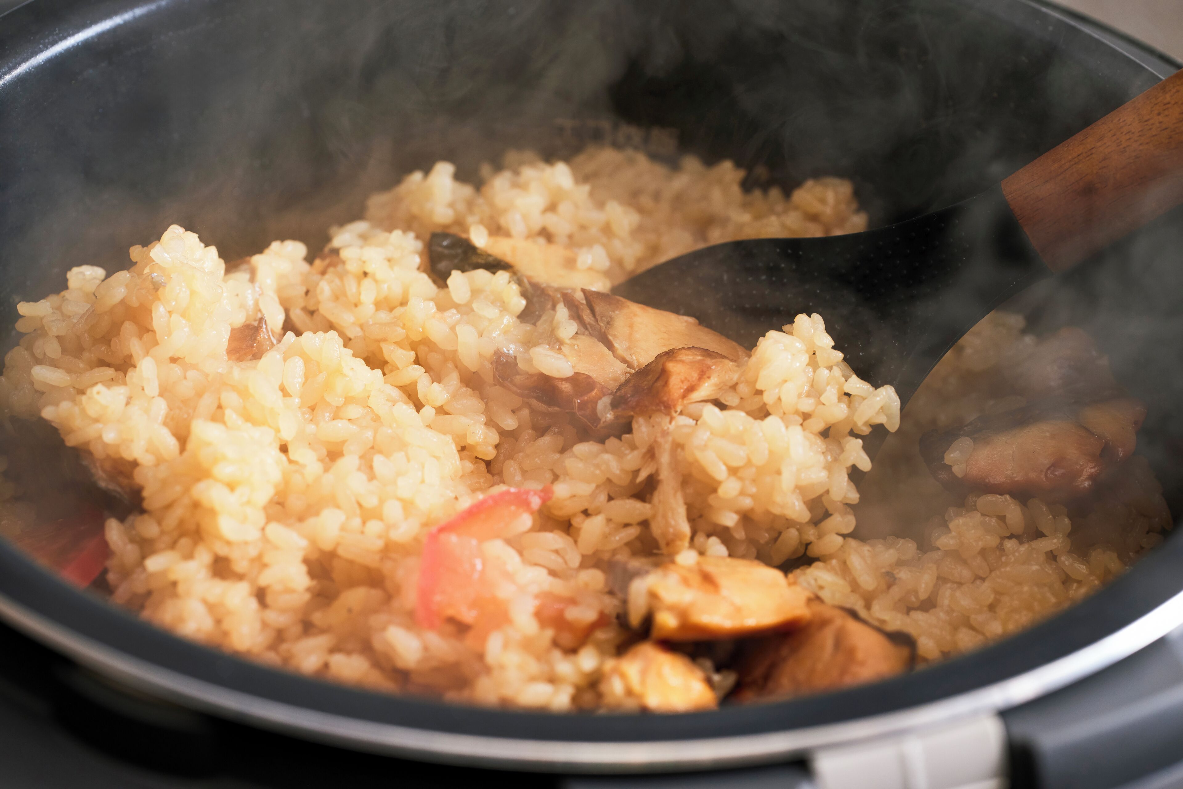 Primer plano de una olla con arroz y pollo, vapor saliendo de la olla.