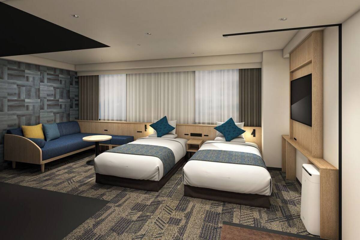 Una habitación de hotel moderna con dos camas, un sofá, una mesita y un televisor.