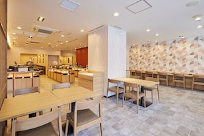 A restaurant interior with wooden tables and chairs, a kitchen area, and a patterned wall. - Hotel MyStays Nagoya - Sakae (Nagoya)