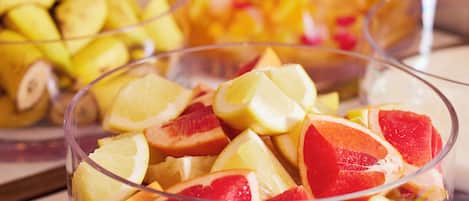 Eine transparente Glasschale mit Fruchtschnitten, darunter Zitrusfrüchte und möglicherweise Grapefruit, vor einem unscharfen Hintergrund mit weiteren Früchten.