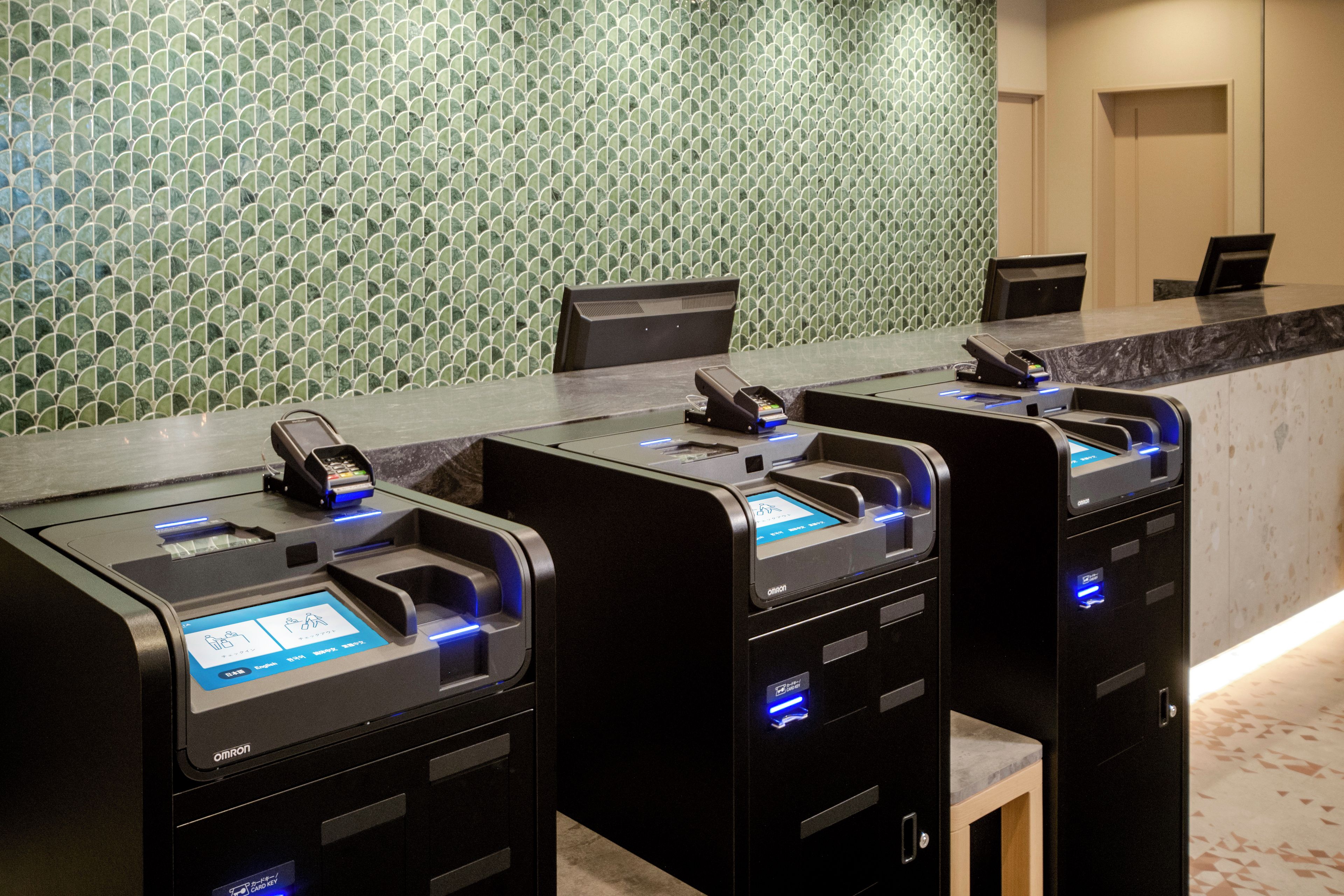 Een rij automaten voor zelfbediening met kaartlezers, een marmeren aanrechtblad en een patroonbehang in de achtergrond.