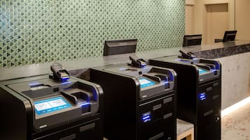 A row of self-service kiosks with card readers, a marble countertop, and a patterned wall in the background.