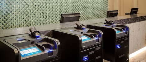 A row of self-service kiosks with card readers, a marble countertop, and a patterned wall in the background.
