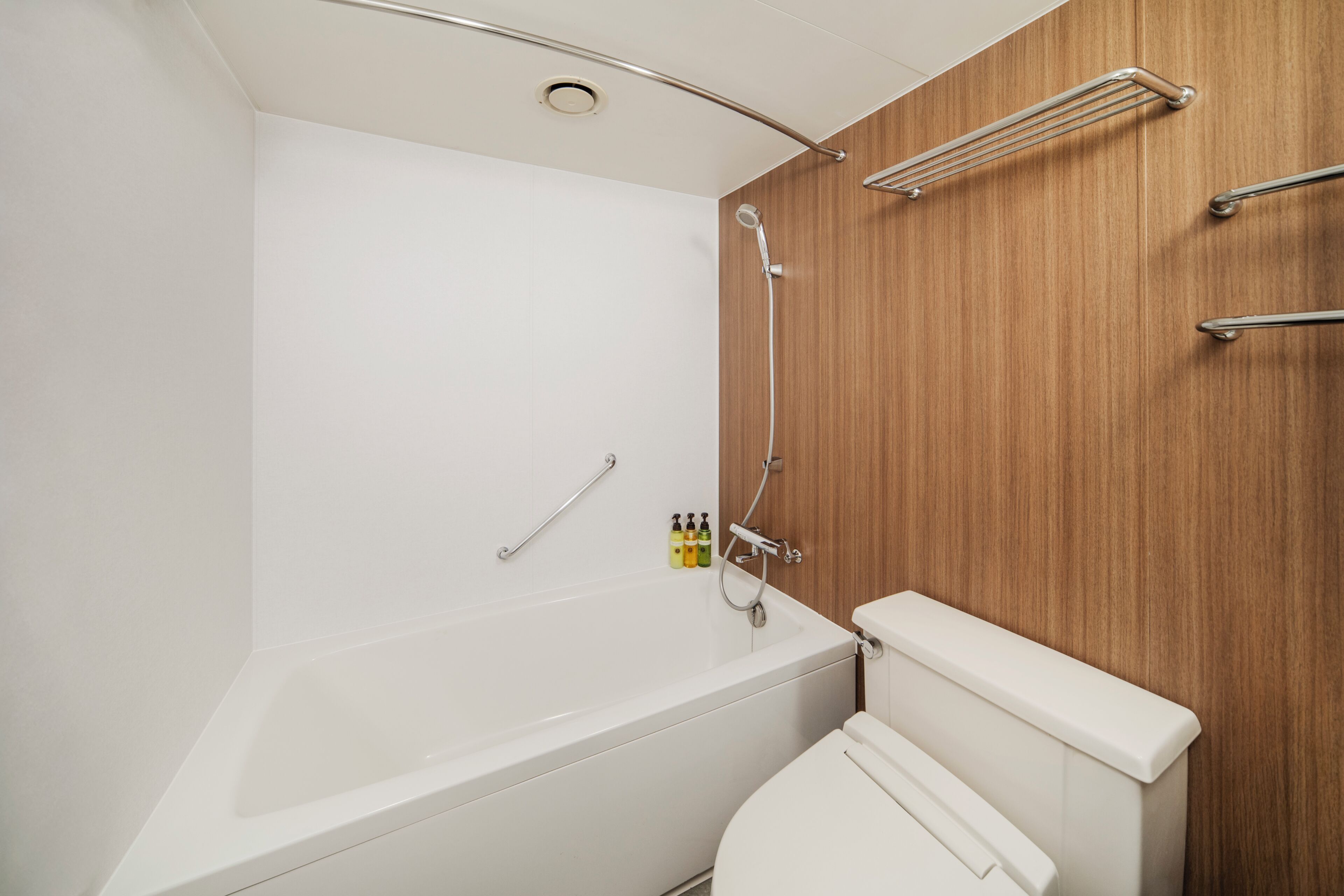 A modern bathroom with a white bathtub, a wooden panel wall, and a white toilet.