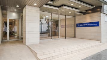 A modern hotel entrance with a glass door, a sign indicating the name 'Hotel Mystays Nagoya Sakae', and a tiled floor.
