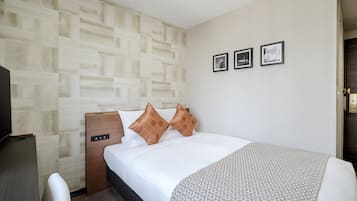 A hotel room with a bed, a desk, a television, and a patterned bedspread.