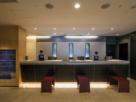 A reception area with a counter, three vertical light fixtures, and a row of red benches.