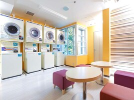 A laundry room with multiple washing machines, a window with a view of greenery, and a seating area with a round table and two chairs.