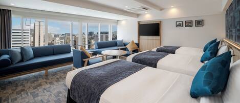 A hotel room with a large window, a sofa, two beds, a TV, and a small table.