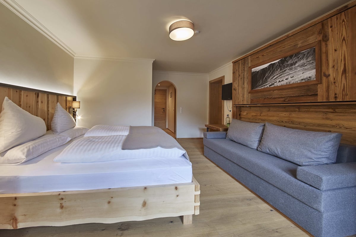 Un dormitorio con cabecera de madera, cama con ropa de cama blanca, un sofá gris y un panel de pared de madera con una imagen.