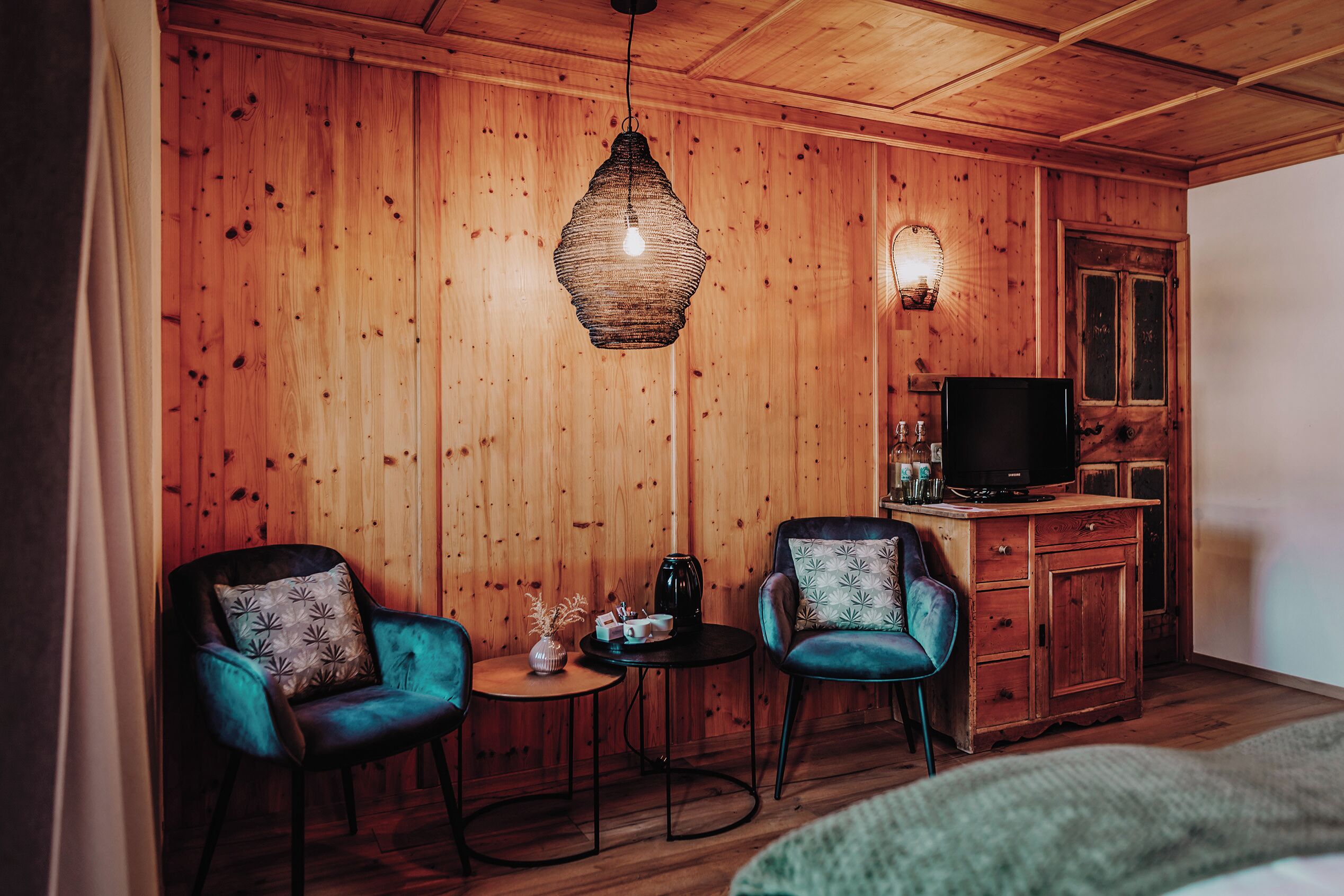 Une pièce chaleureuse avec des murs en bois, un luminaire suspendu, une télévision et deux fauteuils séparés par une petite table.