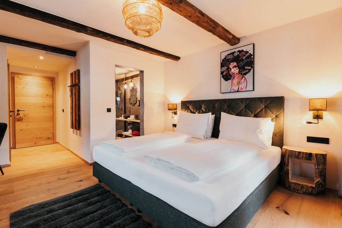 Una habitación de hotel moderna con una cama grande, suelo de madera, armario empotrado y una cabecera original.