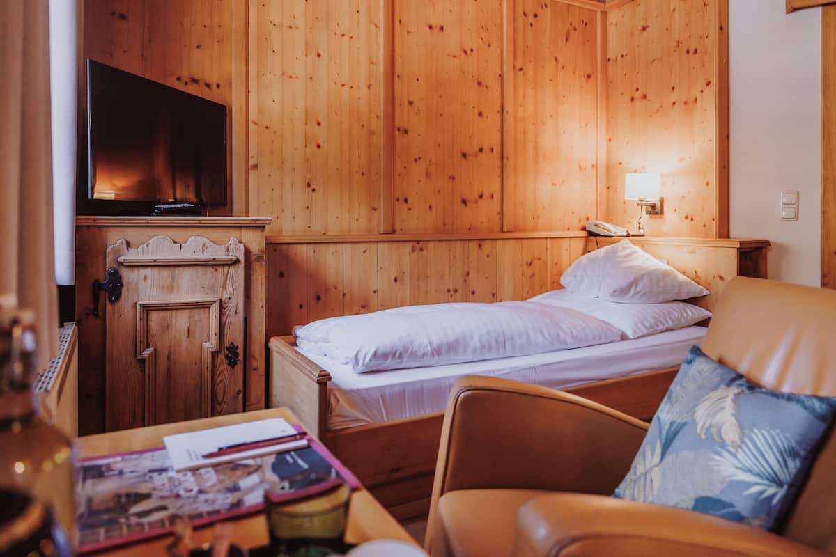 Una habitación con paneles de madera, una cama, un televisor, una mesita de noche y una silla.